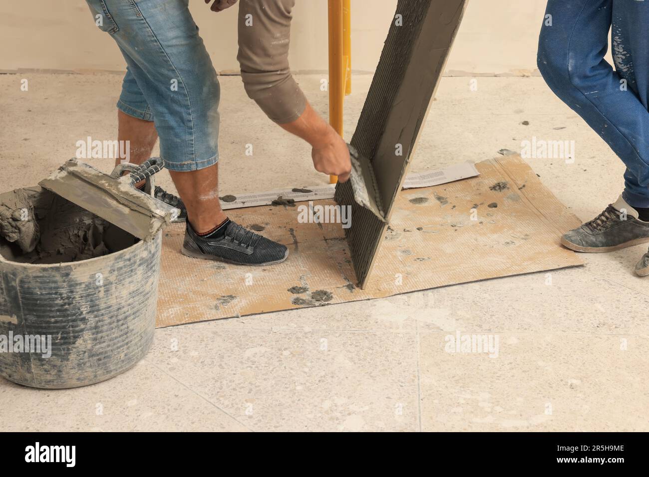 Worker spreading adhesive mix over tile with spatula, closeup Stock Photo