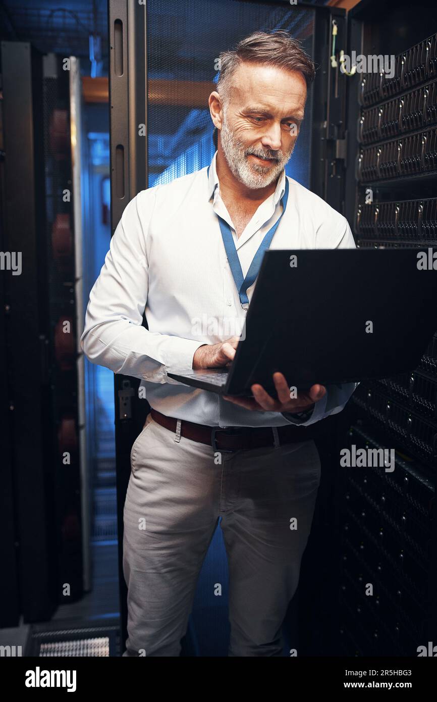 Consider it sorted. a mature man using a laptop while working in a server room. Stock Photo