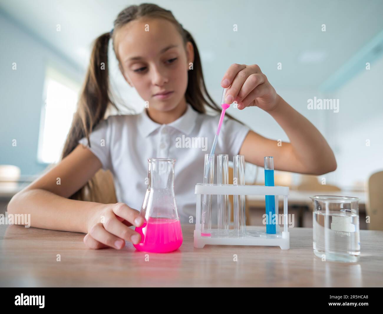 A schoolgirl conducts experiments in a chemistry lesson. Girl pouring ...