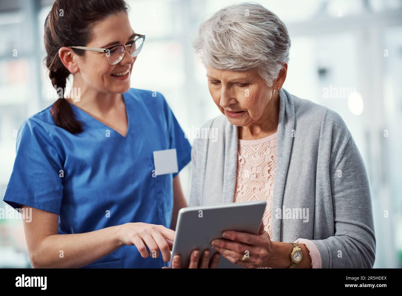 I can access it all from here. a young female nurse and her senior patient looking at a tablet in the old age home. Stock Photo