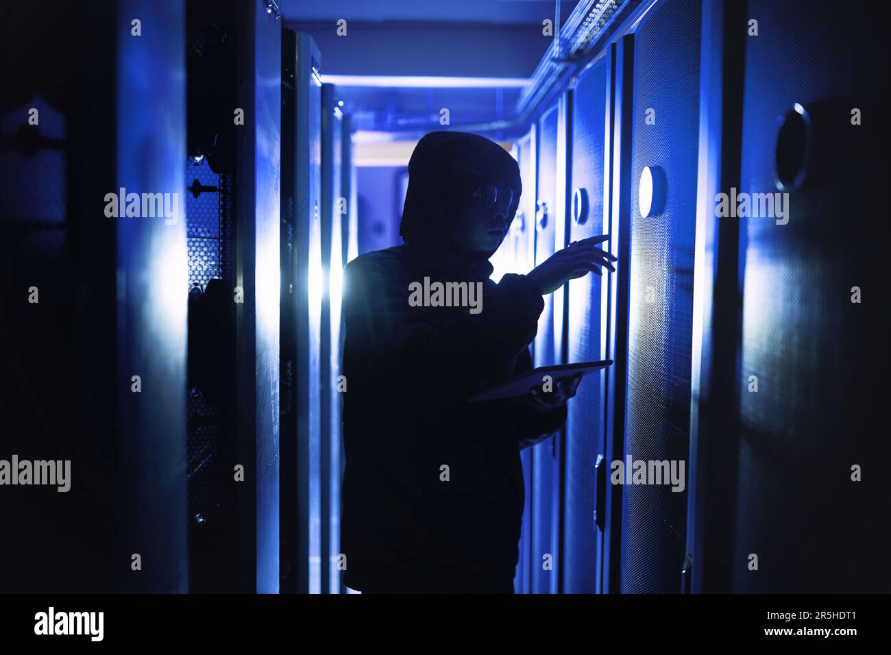Cyber attacks can really sneak up on you. a hacker using a digital tablet in a server room. Stock Photo