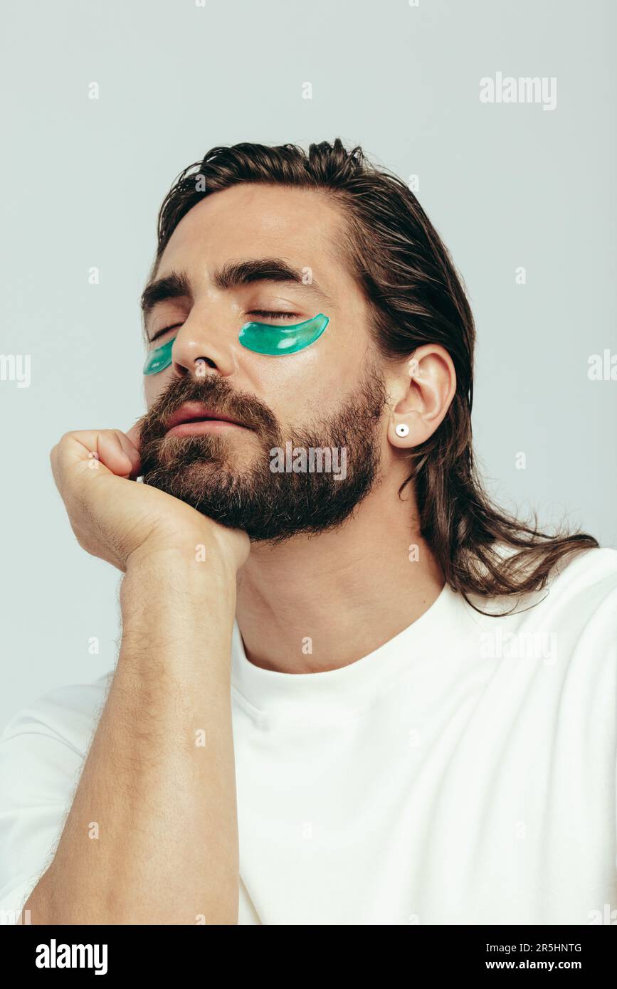 Man practicing skincare and grooming with under eye hydrogel patches in a studio. Confident young man relaxing with his eyes closed, absorbing the ing Stock Photo