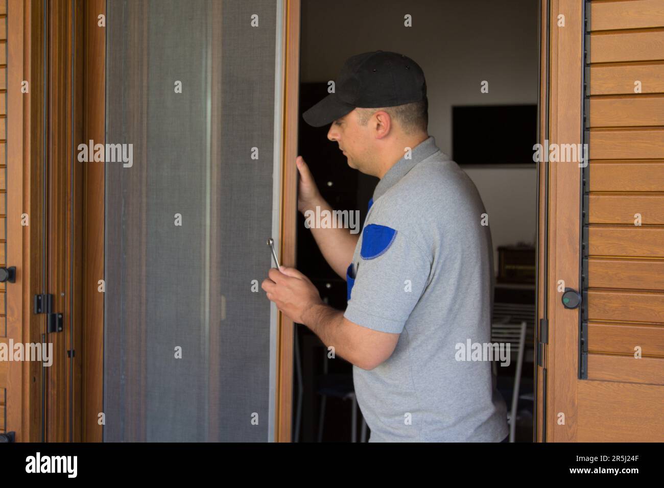 Image of a handyman installing a fly screen in a French window of his house. Protection of the house from insects. Stock Photo