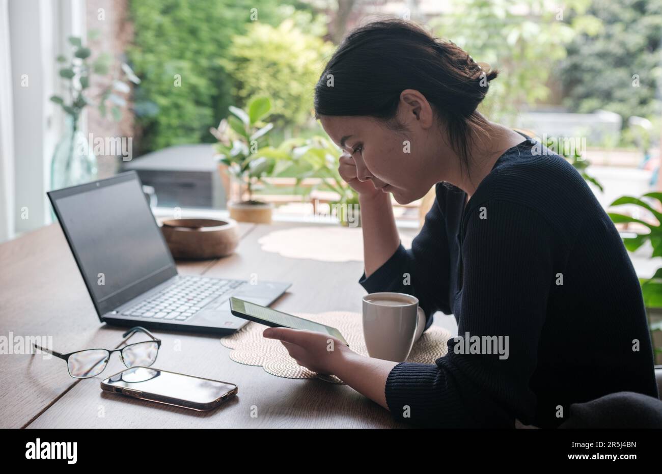 Young Central Asian woman reading her ebook while drinking her coffee. Stock Photo