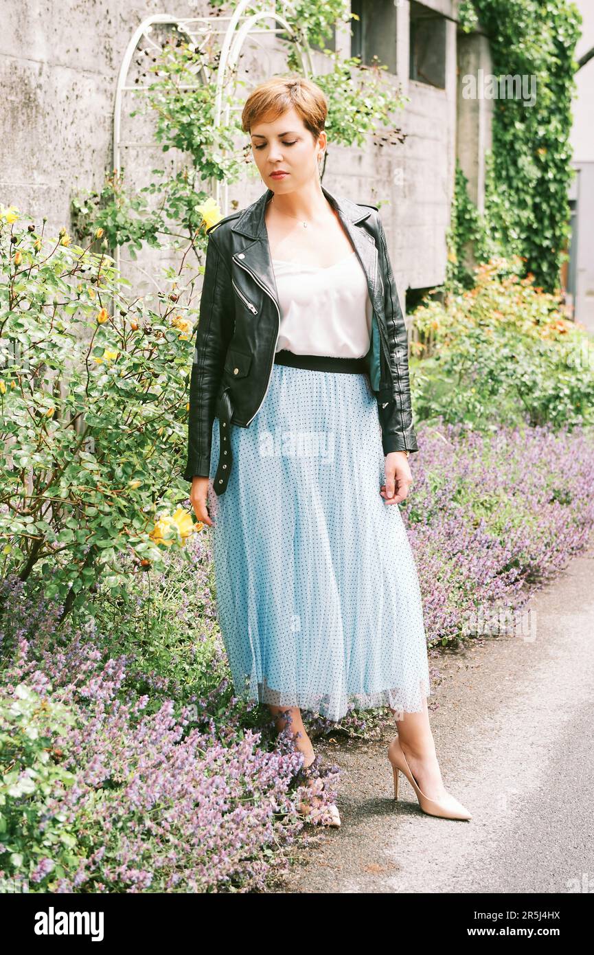Outdoor portrait of beautiful mature woman wearing blue skirt and black leather jacket Stock Photo