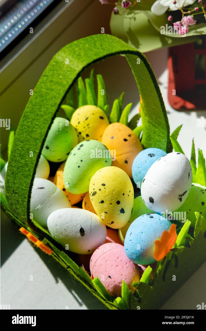 Easter green basket with plastic colored eggs on the windowsill Stock Photo