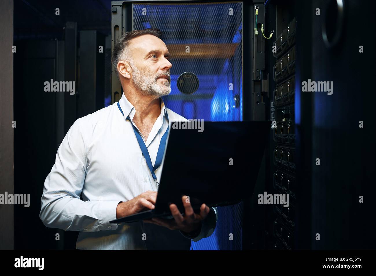 Working on the main connection. a mature man using a laptop while working in a server room. Stock Photo