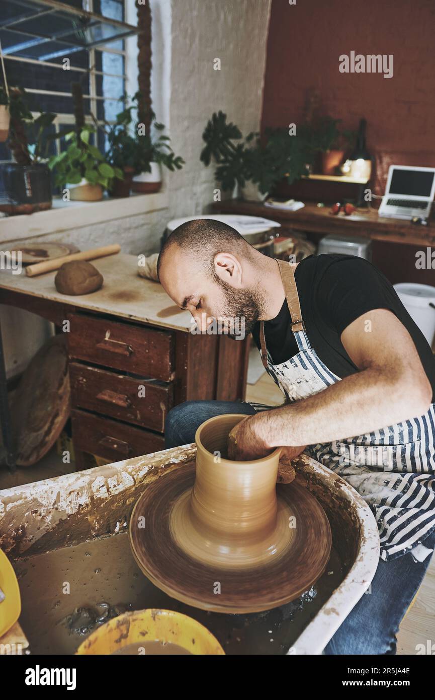 Who said grownups dont play in the dirt. a young man working with clay in a pottery studio. Stock Photo