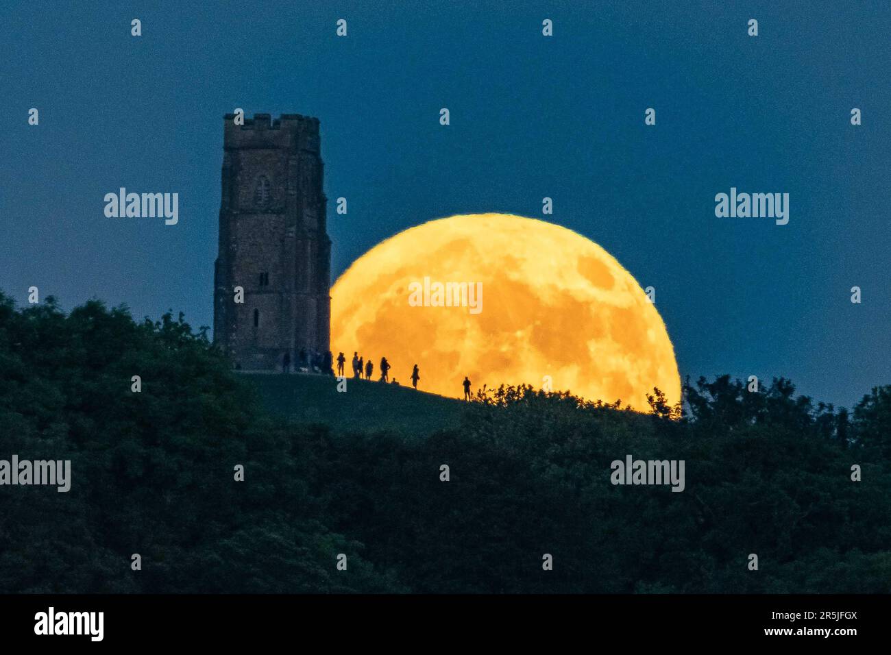 Glastonbury, Somerset, UK.  3rd June 2023.  UK Weather.  The full Strawberry moon rises up from behind St Michael’s Tower on Glastonbury Tor in Somerset as a crowd of people gather on top of the hill to watch.   Picture Credit: Graham Hunt/Alamy Live News Stock Photo