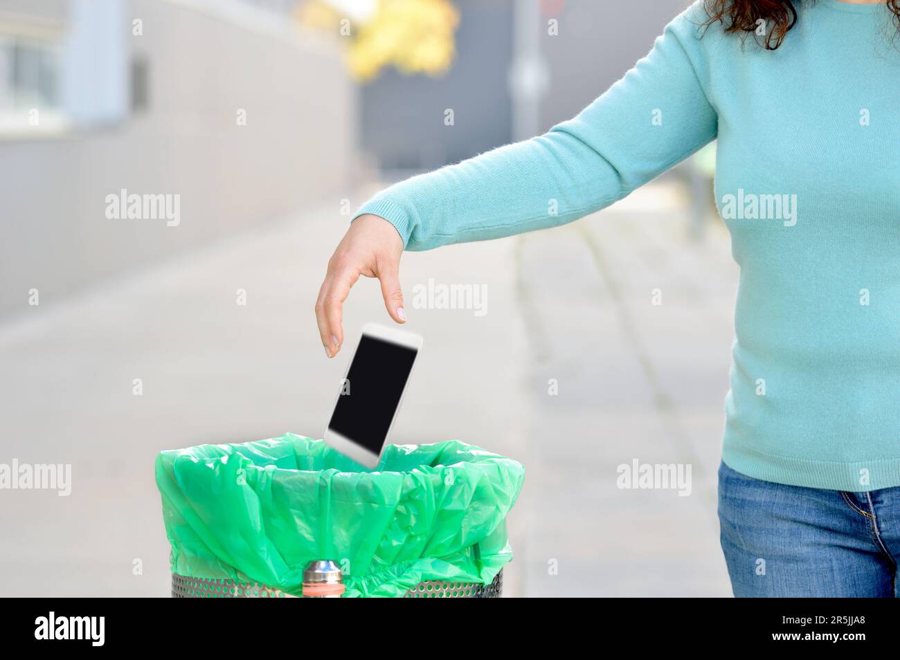 Woman throwing her broken phone into the garbage in a trash bin at