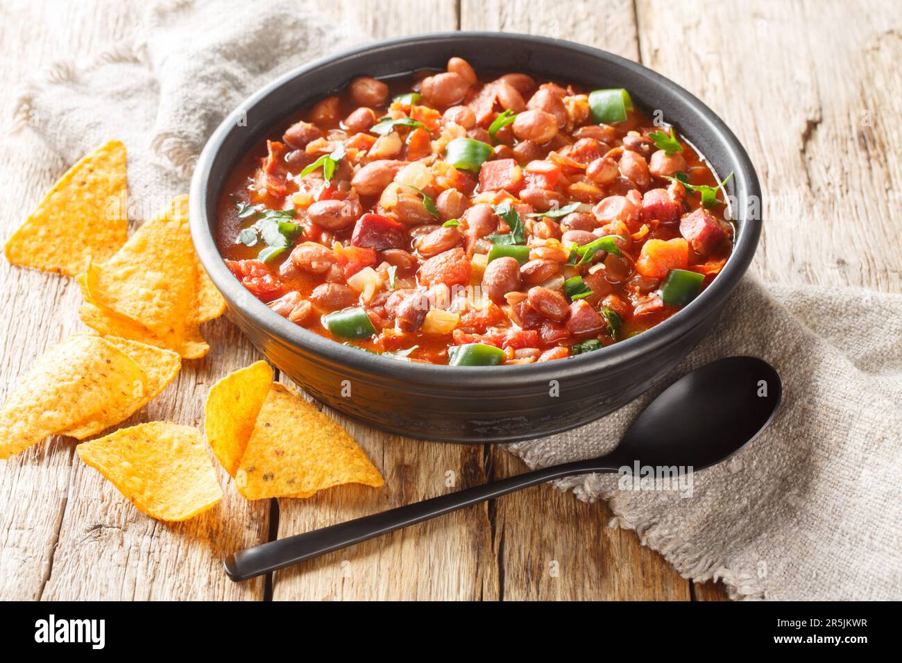 Mexican pinto bean stew with tomatoes, sausages, bacon and onions close-up on a bowl on the table. horizontal Stock Photo