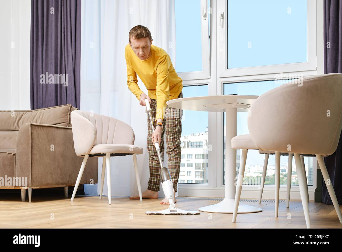Middleaged man washing floor with mop barefoot doing housework in