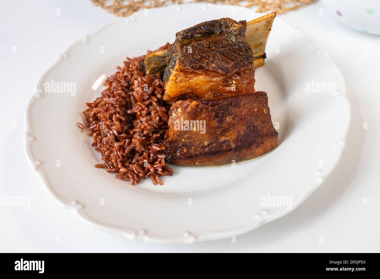 Baked beef rib with red rice on white plate on white background. Stock Photo