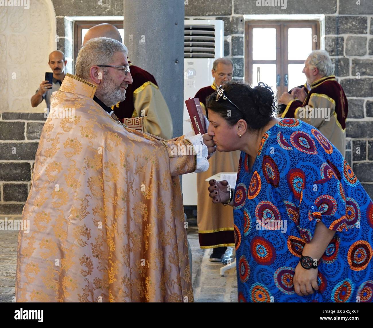 A woman kisses a Bible in the hands of Senior Priest Abraham Firat after the ritual at Diyarbak?r Surp Hovsep Church. At the Surp Hovsep Armenian Catholic Church, which was heavily damaged in clashes between armed Kurdish PKK militants and Turkish security forces in the center of Diyarbakir in 2015 and repaired as a result of a 4-year restoration, the second ritual in the last 100 years after the first ritual in 2021. Very few Armenians who came from Istanbul and lived in Diyarbakir attended the ceremony. The ritual was led by Senior Priest Abraham Firat and Subordinate Deacon Jan Acemoglu, wh Stock Photo