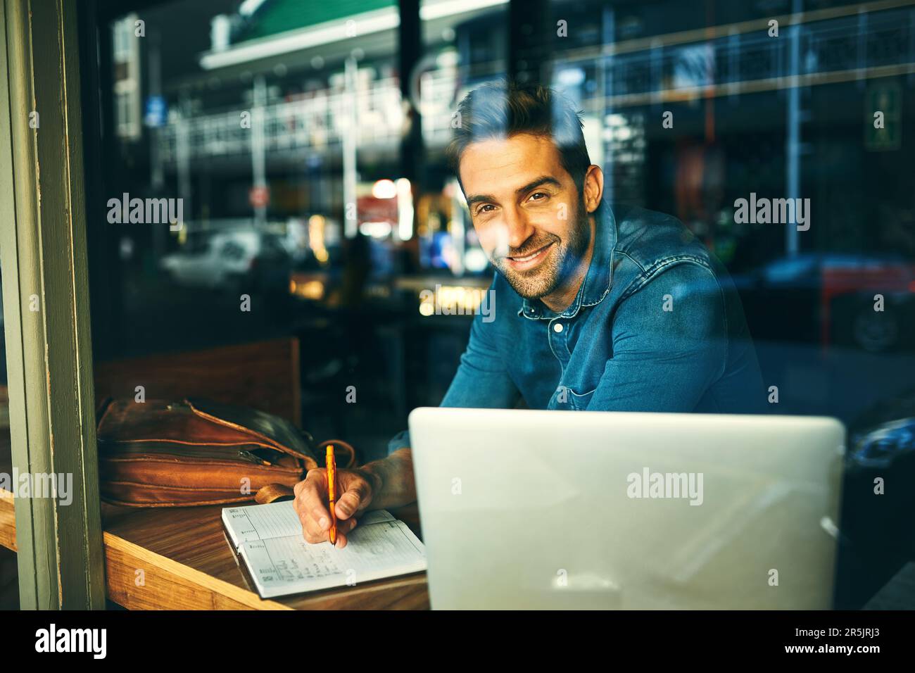 I love working in this cafe. Cropped portrait of a handsome young businessman sitting in a cafe alone and writing in a notebook. Stock Photo