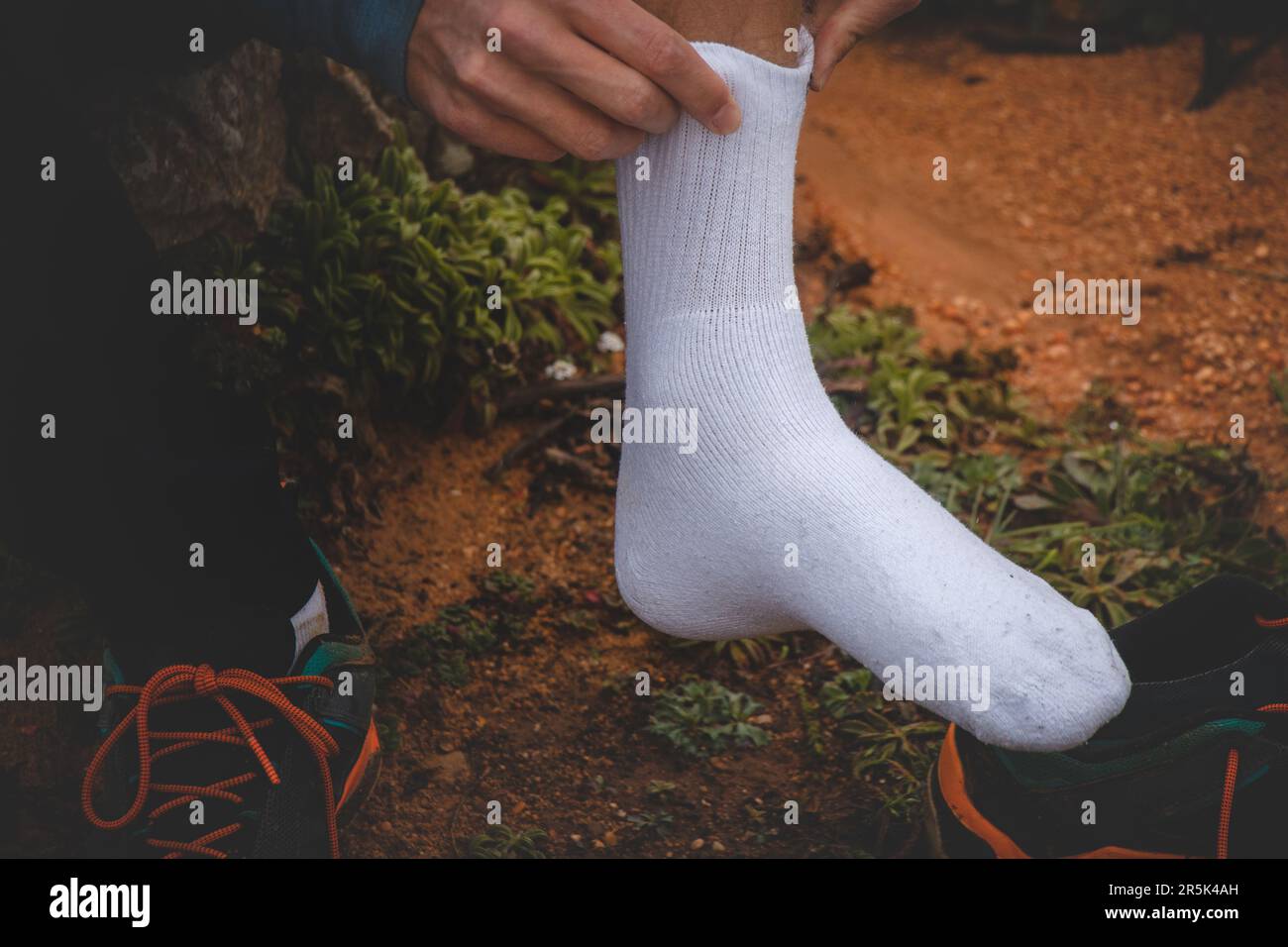 young traveler on his pilgrimage along the Fisherman Trail patches up his ankle blisters and puts on a new sock. The hardships of long journeys. Stock Photo