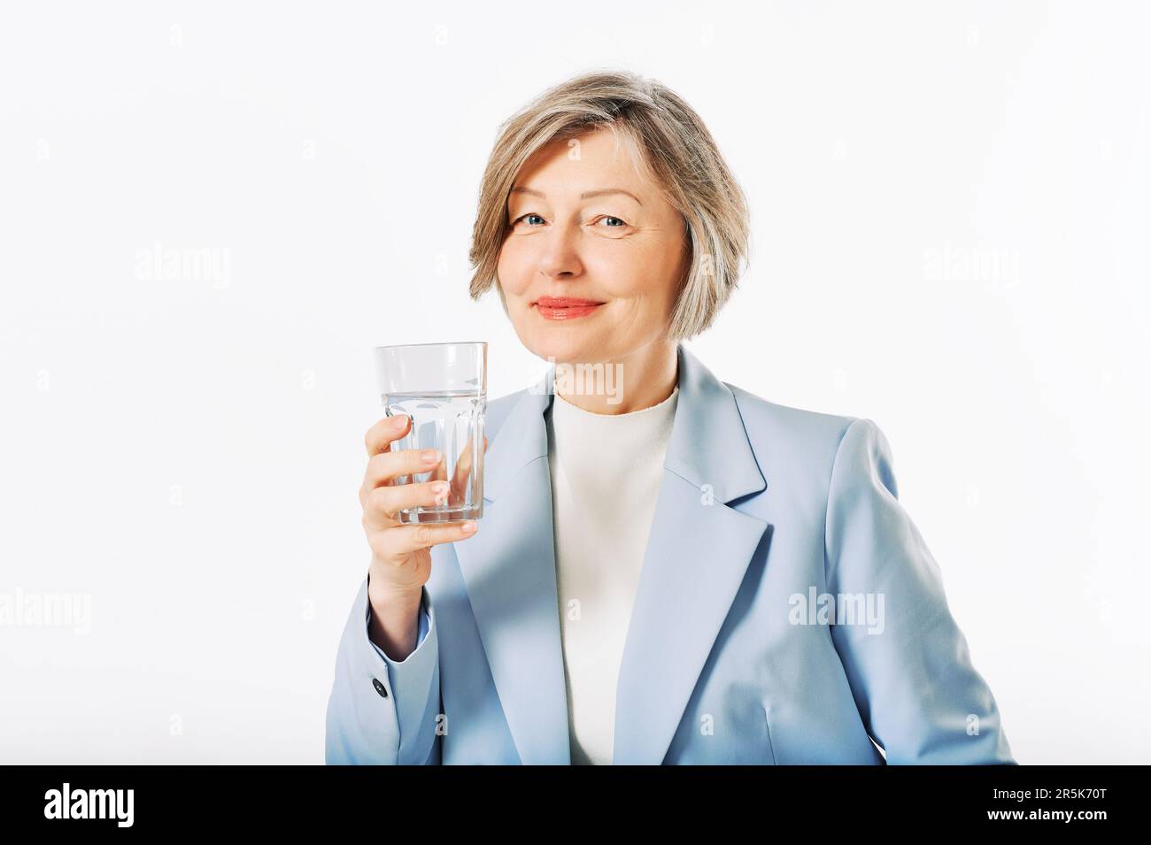 Studio portrait of middle age woman posing on white background, 55 - 60 year old female model holding glass of water Stock Photo