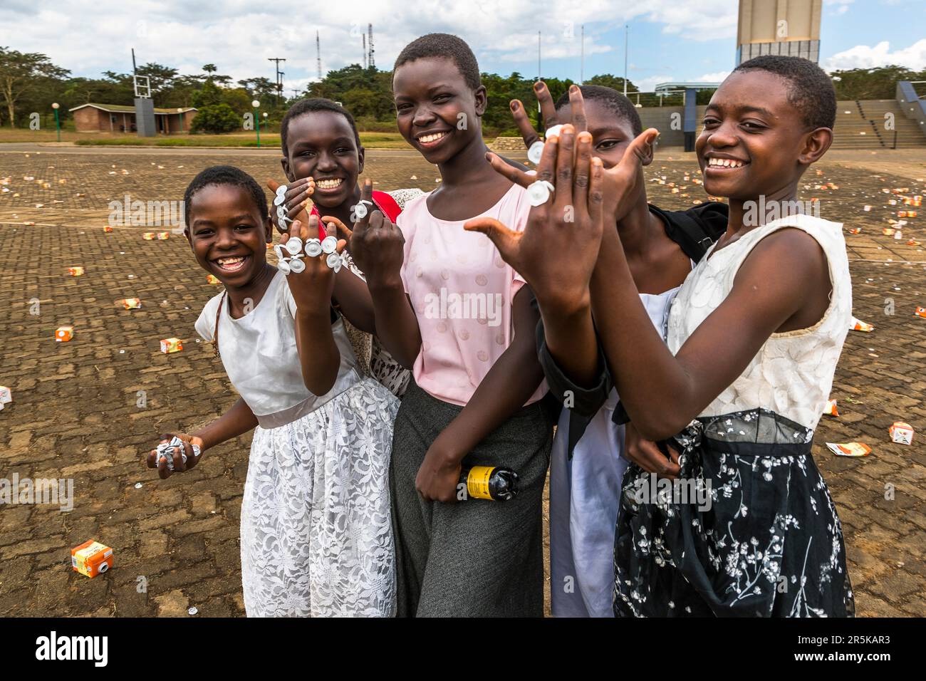 Posing with jewelry made of plastic. Here girls in front of the Memorial War Tower in Lilongwe after a public function. Young girls collect the cap rings of the maheu packs discarded on the national holiday in honor of Malawi's first president (Hastings Kamuzu Banda) to make jewelry. Maheu or Mahewu is a typical drink in Malawi made from fermented maize. Lilongwe, Malawi Stock Photo