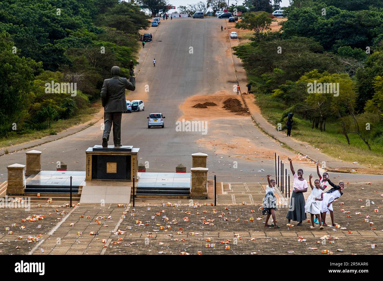 View of Hastings Kamuzu Banda memorial from Memorial War Tower. Girls collect lying plastic parts and wave. Young girls collect the cap rings of the maheu packs discarded on the national holiday in honor of Malawi's first president (Hastings Kamuzu Banda) to make jewelry. Maheu or Mahewu is a typical drink in Malawi made from fermented maize. Lilongwe, Malawi Stock Photo