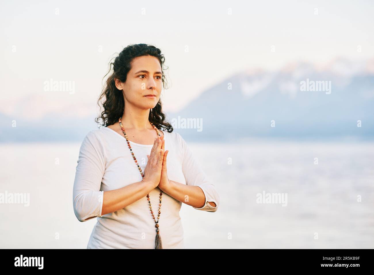 Beautiful spiritual woman meditating by the lake, wearing white clothes ...