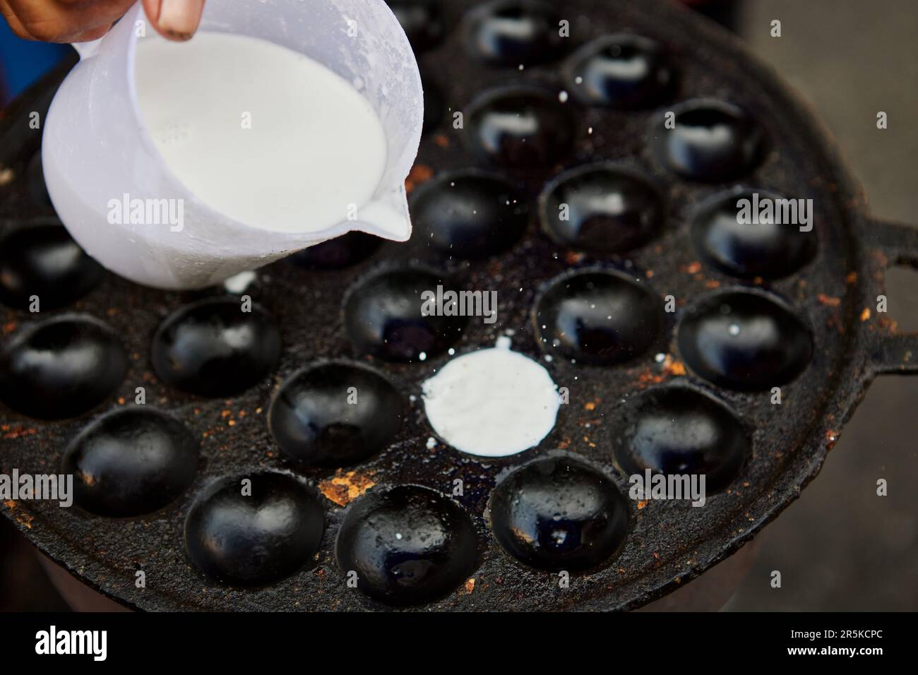 Cropped hand pouring coconut-rice pancakes into a pan Stock Photo