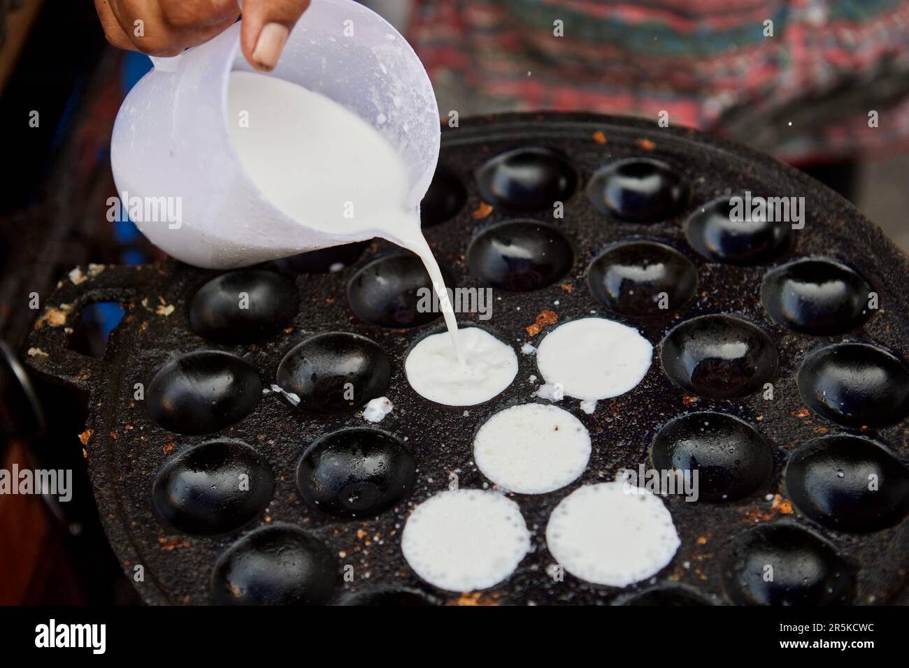 Cropped hand pouring coconut-rice pancakes into a pan Stock Photo