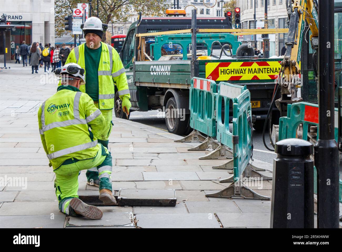 Two maintenance workers lifting an inspection cover in the pavement in the Strand, Charing Cross