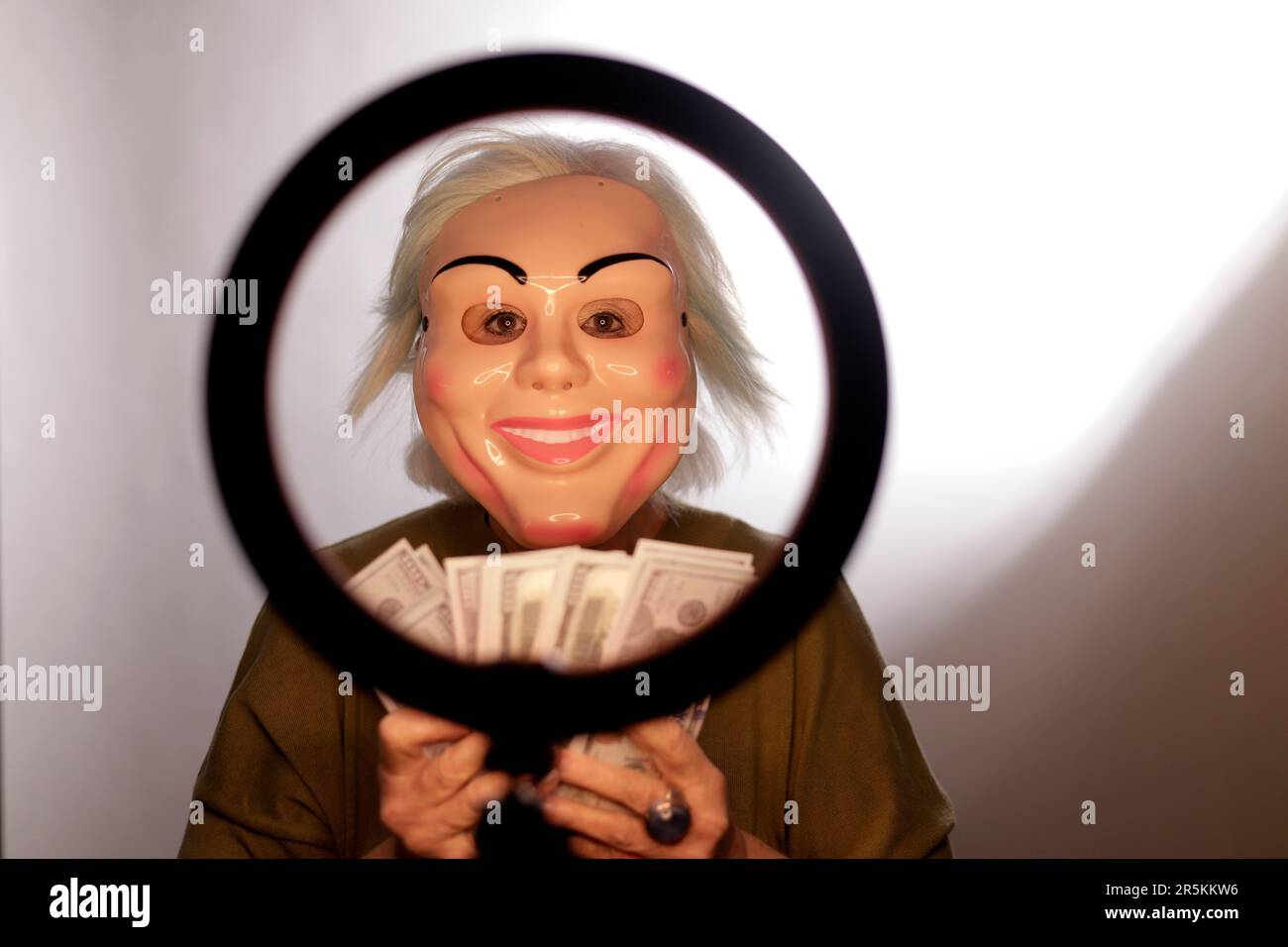woman with mask in front of light ring showing money Stock Photo