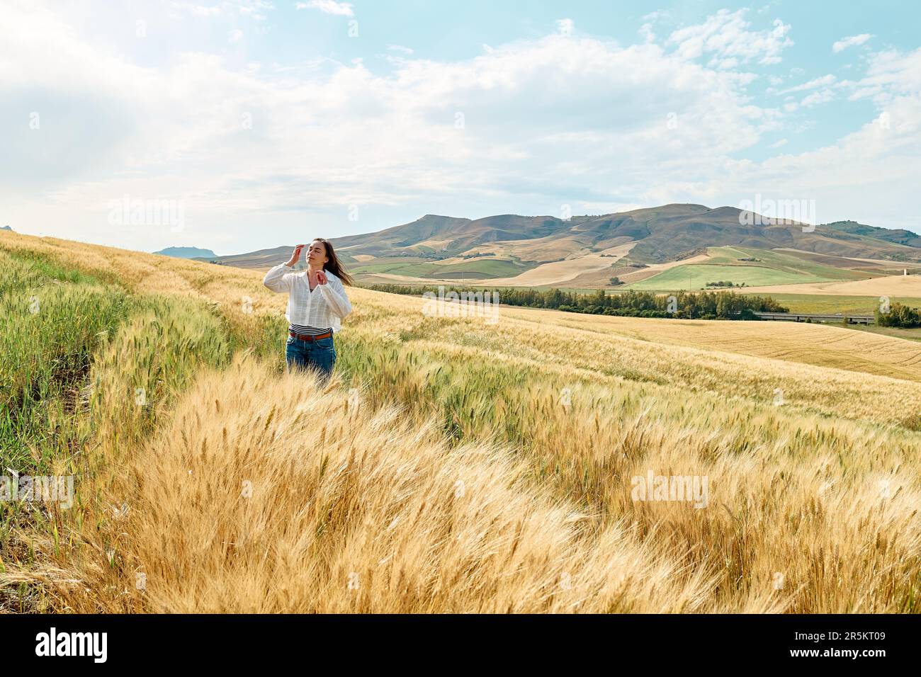 Woman walking in golden wheat field in hot summer sun and blue sky with ...