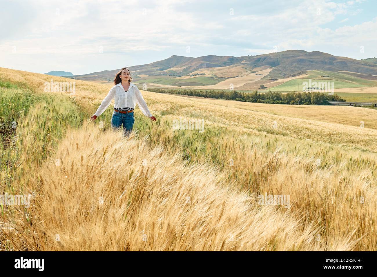 Woman walking in golden wheat field in hot summer sun and blue sky with ...