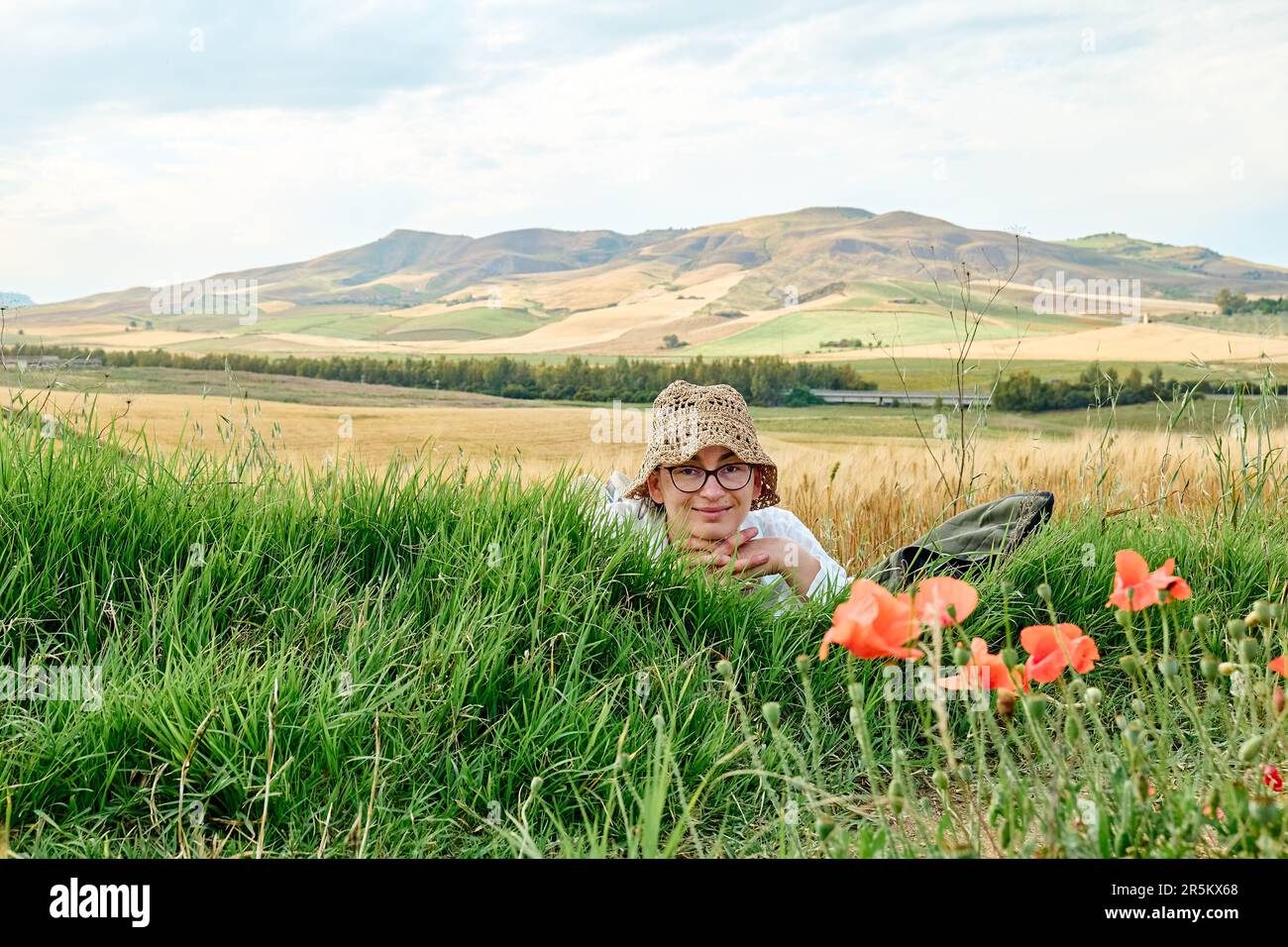 Smiling woman in straw hat and glasses lying in poppies meadow near ...