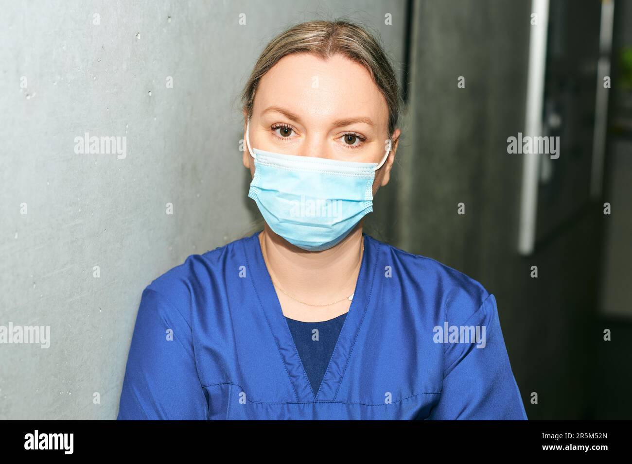Young female scrub nurse wear blue uniform and face mask, standing in
