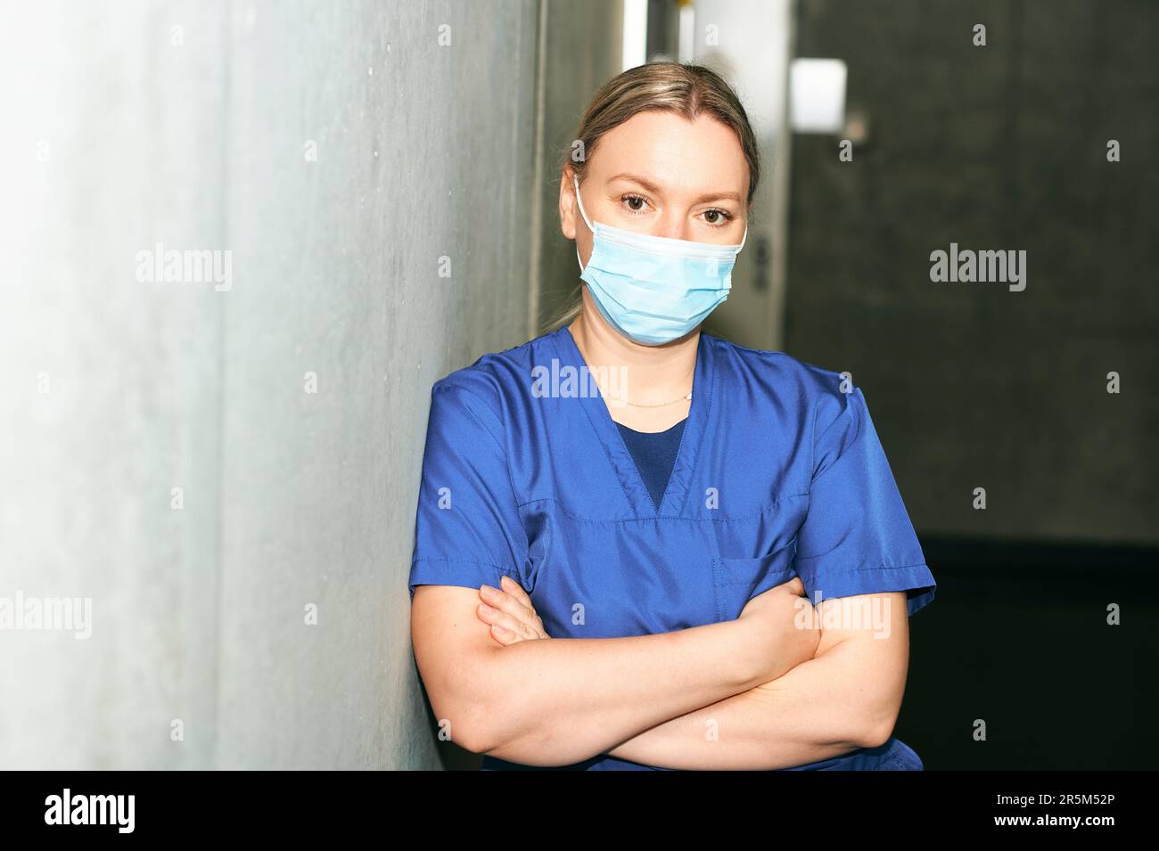 Young female scrub nurse wear blue uniform and face mask, standing in