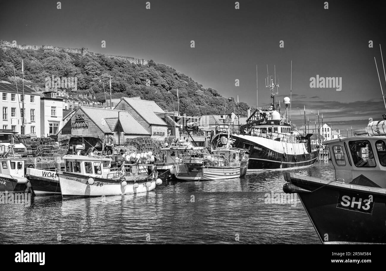 The harbour and town at Scarborough.  Boats are moored in the harbour with the waterfront behind. Castle ruins are on the hill above and the bow of a Stock Photo