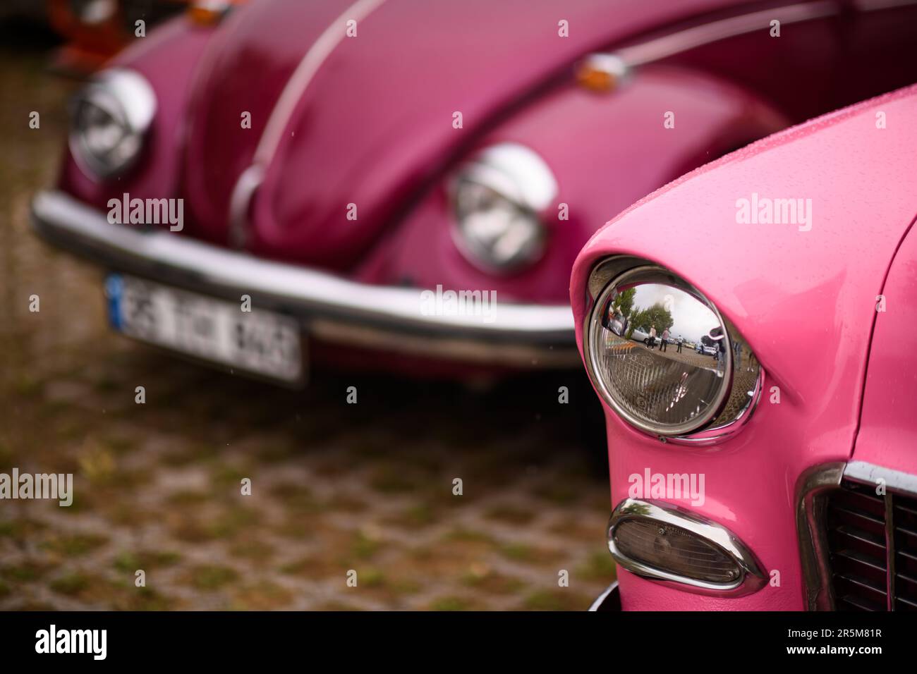 Izmir, Turkey - June 3, 2023: Close-up focus on the headlight of a pink 1955 Chevrolet Bel Air with a soft-focus background featuring a 1972 pinkish-p Stock Photo