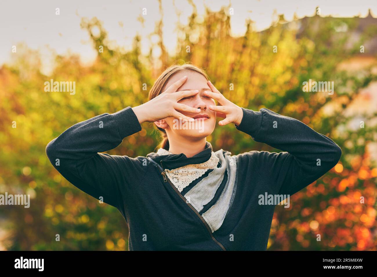 Outdoor portrait of young teen girl in golden light, hiding face with hands Stock Photo