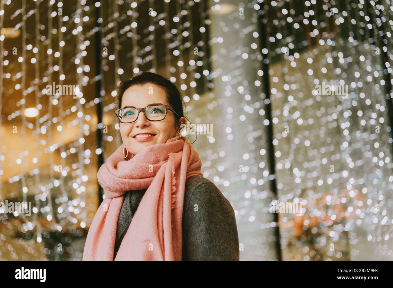Outdoor portrait of beautiful woman posing ina city with many lights on background, wearing glasses and pink scarf Stock Photo