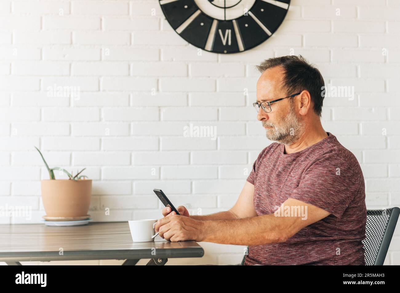 Middle age man relaxing on balcony, drinking cofee, using smart phone Stock Photo