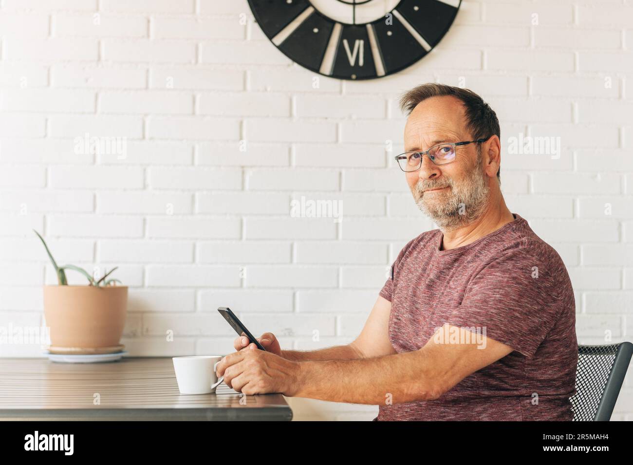 Middle age man relaxing on balcony, drinking cofee, using smart phone Stock Photo