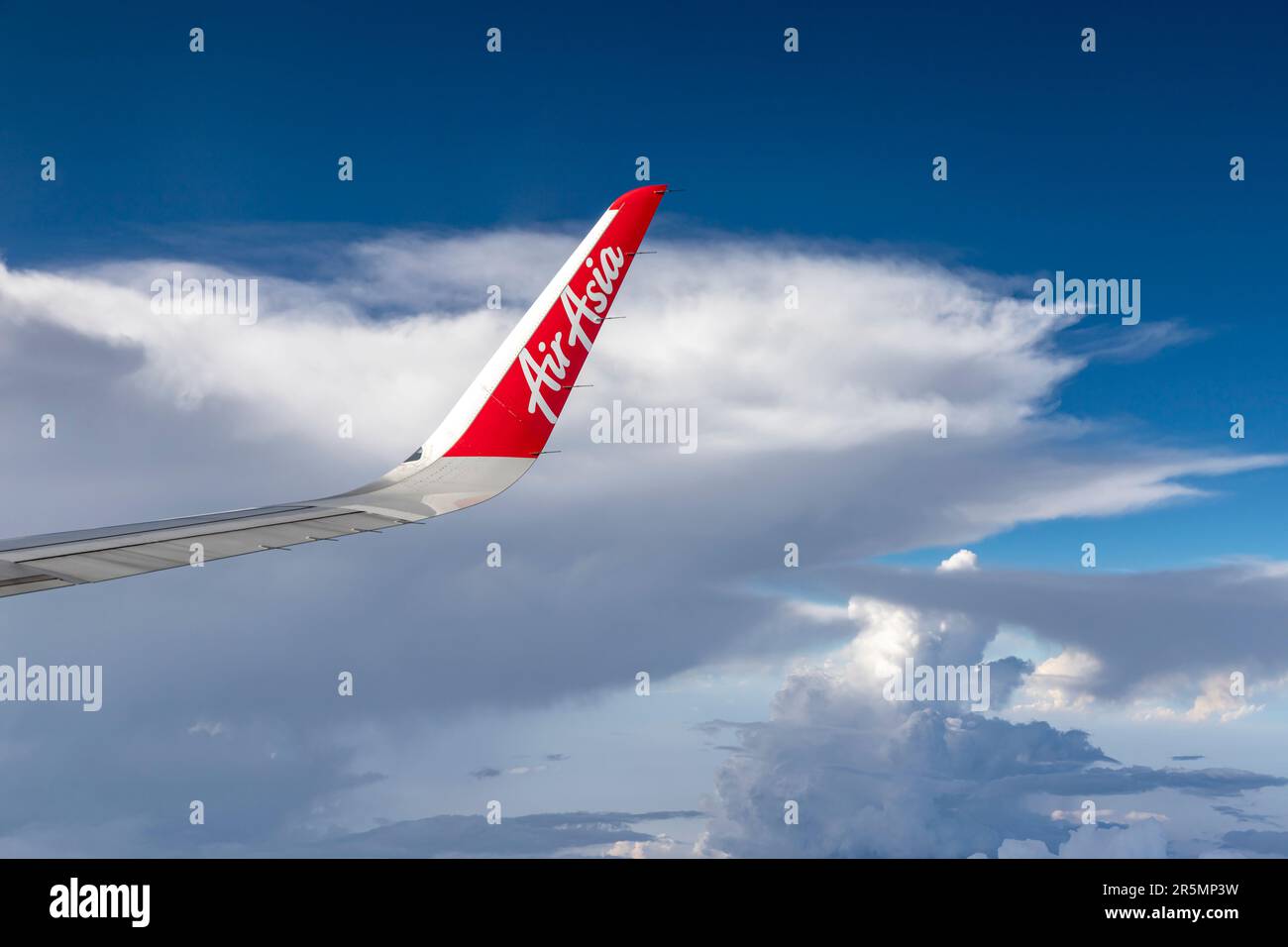Bangkok Thailand - March 30, 2019: The trademark logo on the wing of AirAsia, a popular low-cost airline in many countries, is soaring in the sky agai Stock Photo