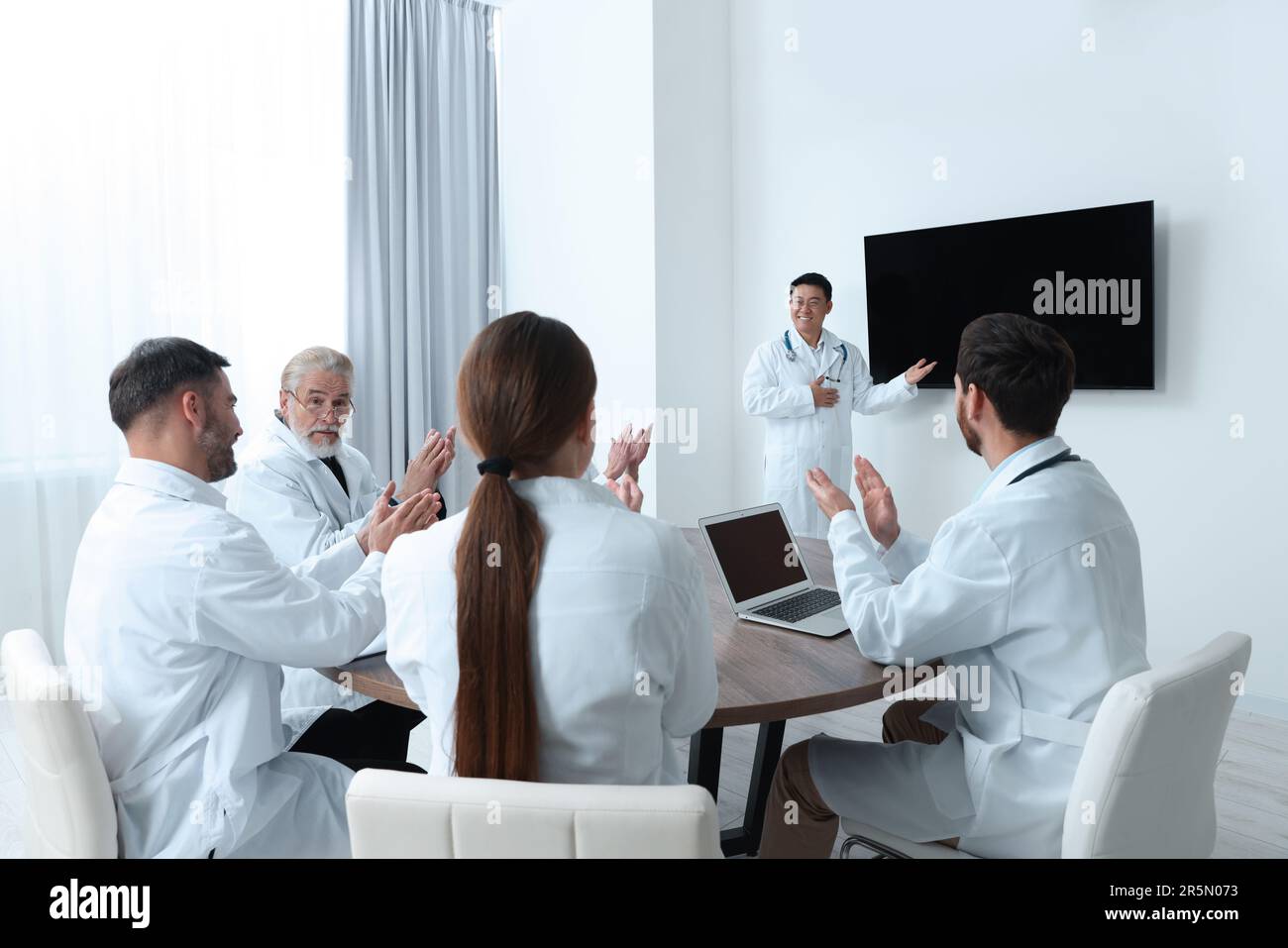 Team of doctors listening to speaker report near tv screen in meeting