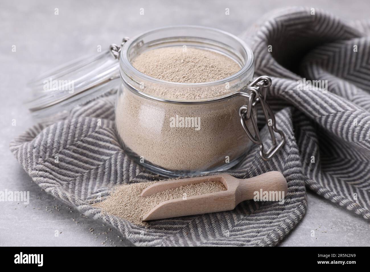 Glass jar and scoop with active dry yeast on light grey table, closeup