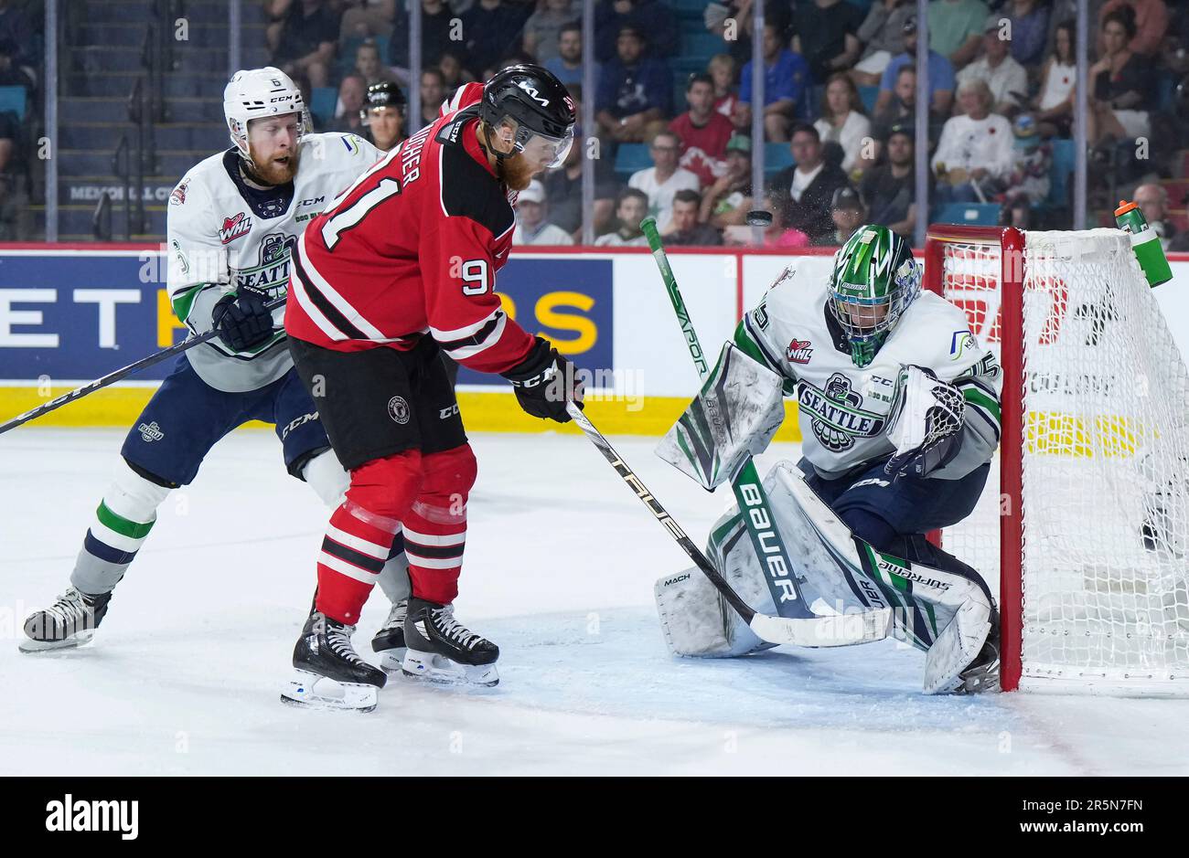 The puck deflects off the mask of Seattle Thunderbirds goalie Thomas Milic, right, as Quebec Remparts Nathan Gaucher (91) and Thunderbirds Luke Prokop (6) watch during second-period CHL Memorial Cup final hockey