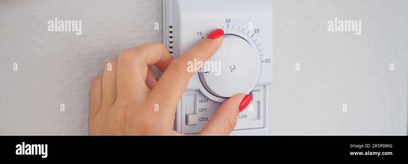 Woman hand adjusts or turns on wall temperature controller controller button Stock Photo