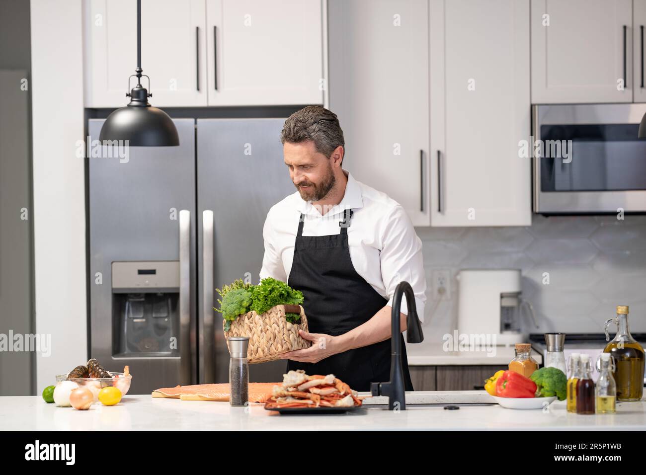 photo of man cooking healthy food. man cooking healthy food. man cooking healthy food wearing apron. man cooking healthy food in the kitchen. Stock Photo