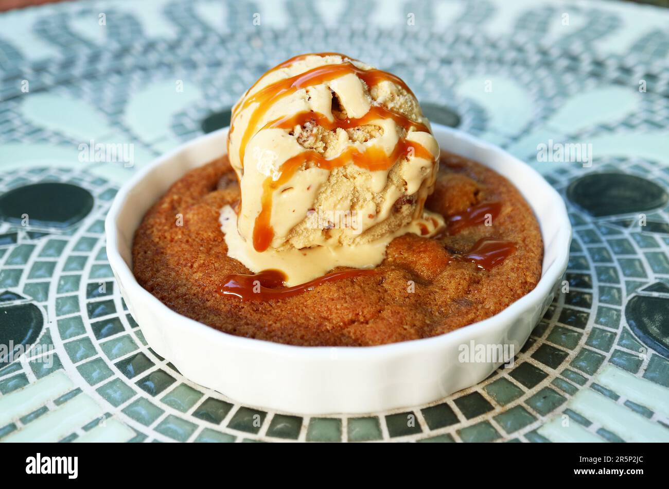 Plate of Warm and Flavorful Skillet Cookie Topped with Ice Cream and Salted Caramel Sauce Stock Photo