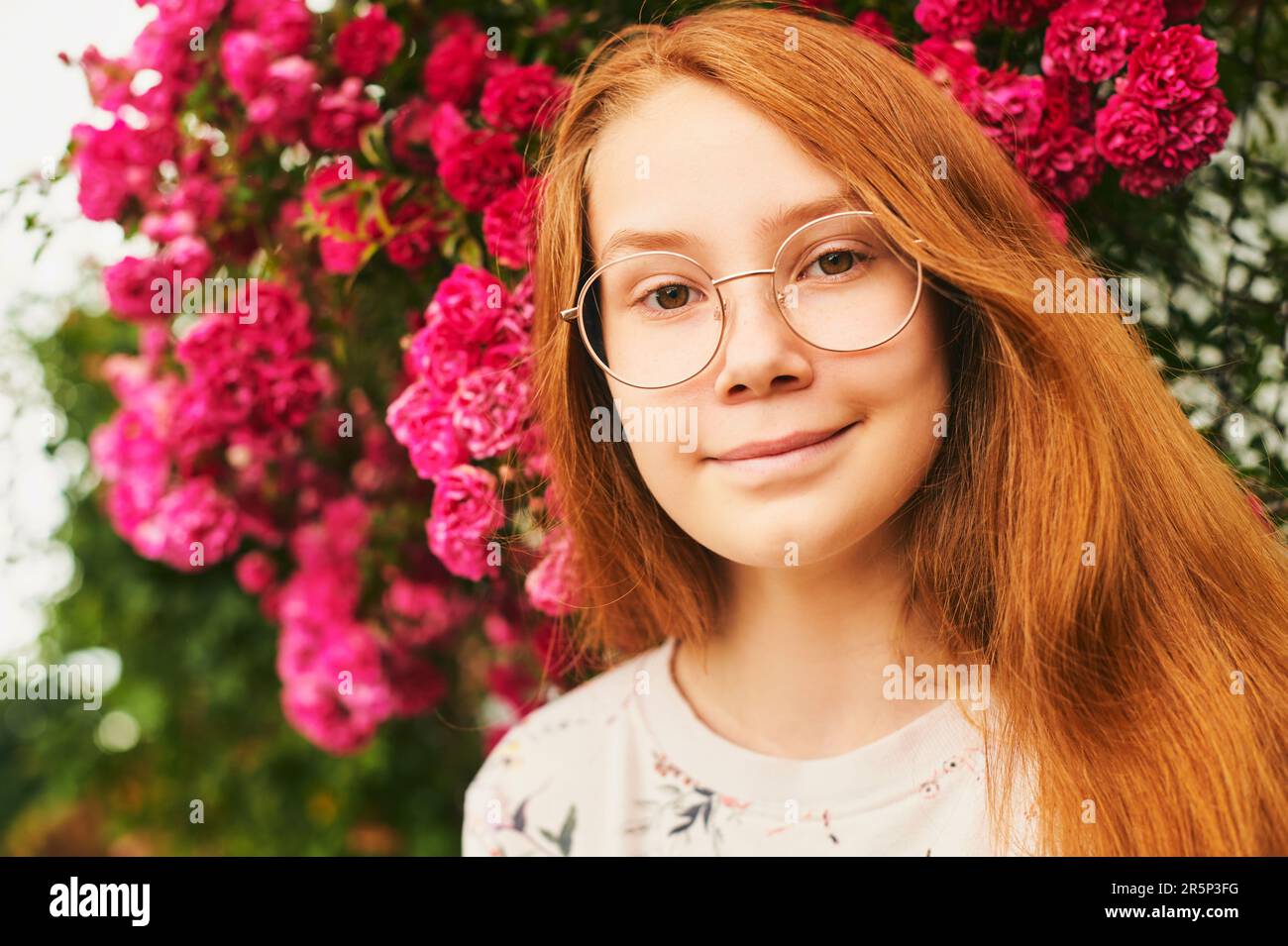 Outdoor close up portrait of happy young girl, wearing eyeglasses, posing in flower garden Stock Photo