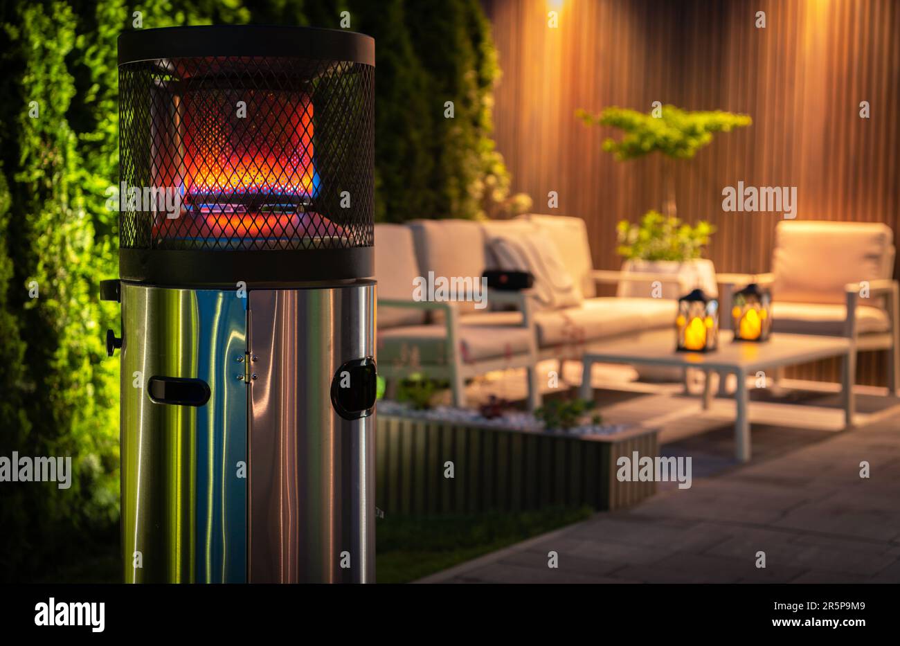 Outdoor Patio Propane Gas Heater For Cold Evenings in Garden Area. Burning Heater in Front of Outdoor Relaxing Area During Night Time. Stock Photo
