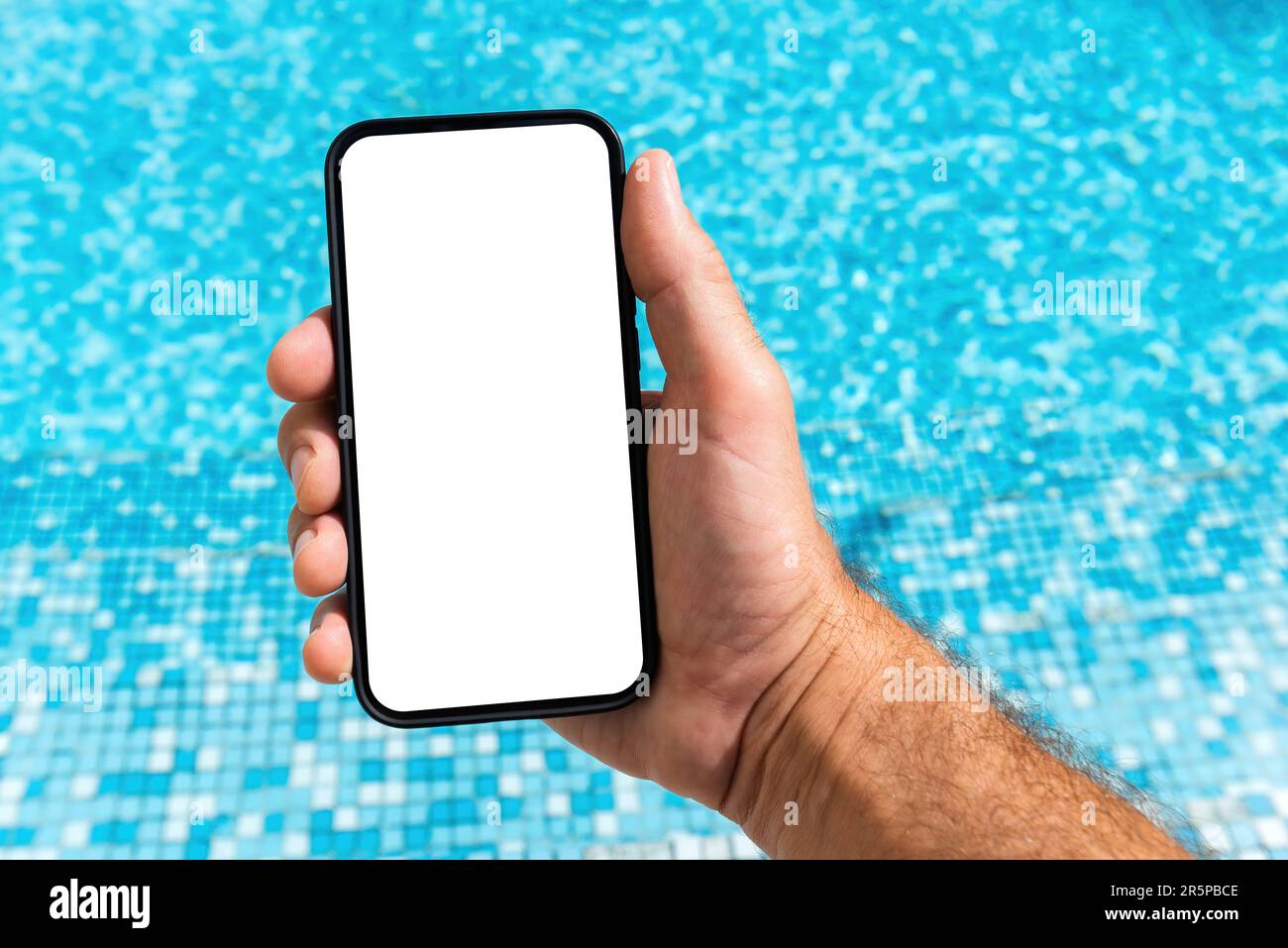 Man holding mobile smart phone with blank mockup screen above the clean outdoor swimming pool water in summer, selective focus Stock Photo