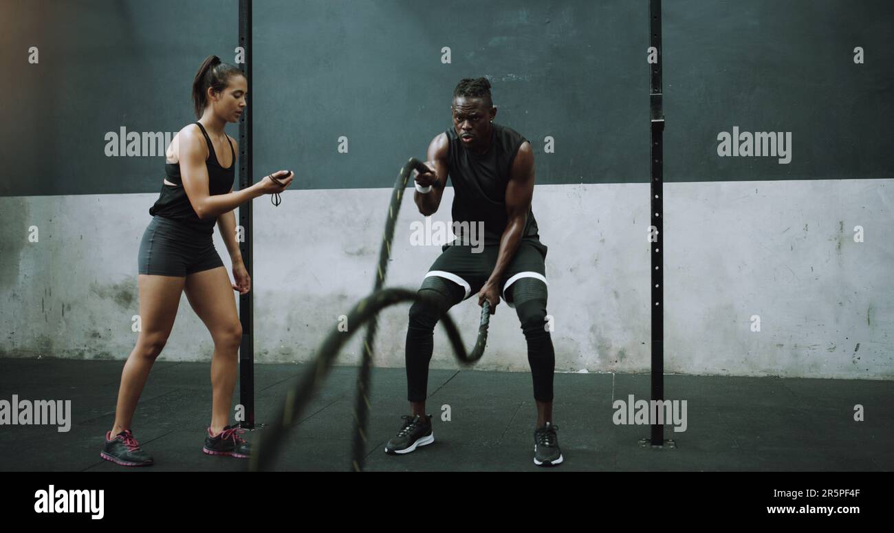 Battle rope, exercise and man with personal trainer and stopwatch at ...